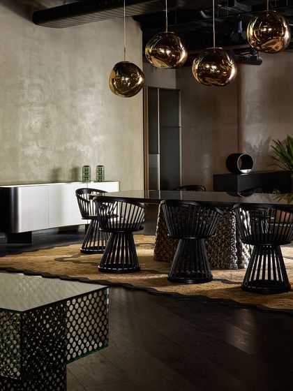 This dining area showcases black wireframe chairs and a table with a sculptural base. The hanging metallic globe lights add a touch of glamour and reflect the surrounding space.
