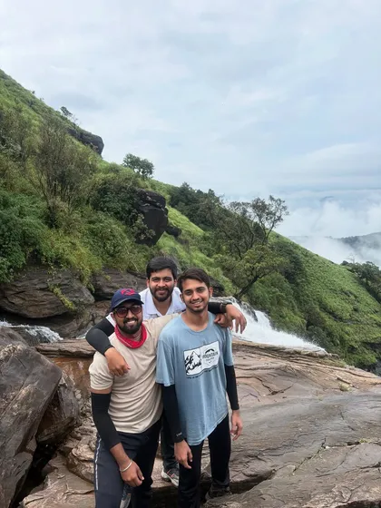 Three friends posing on a rock at the top of Bandaje Falls, with the valley stretching out behind them.