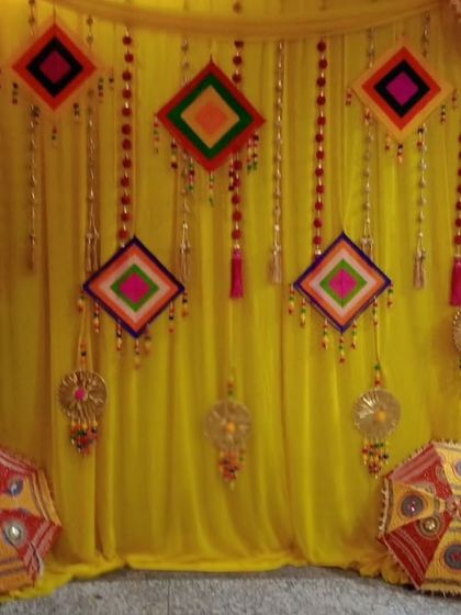 A close up view of a Haldi backdrop focusing on the decorative elements. You can see the colorful thread-work hangings and Rajasthani umbrellas I use to bring an authentic, handcrafted feel to the celebration.
