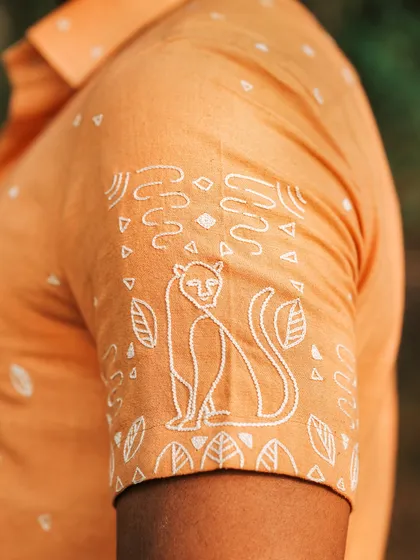The sleeve detail of our tangerine orange shirt, featuring a hand-embroidered panther line drawing. It's crafted for those who approach life with ferocity and appreciate refined dominance in their style.