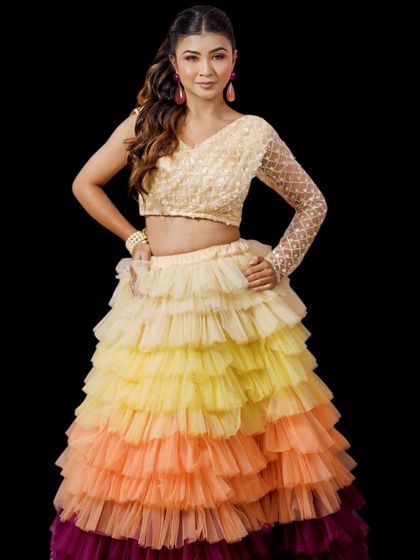 Live your Barbie moment with this fun and vibrant tiered lehenga. The skirt features layers of ruffles in shades of yellow, orange, and pink, paired with a one-shoulder sequined blouse for a playful Sangeet look.