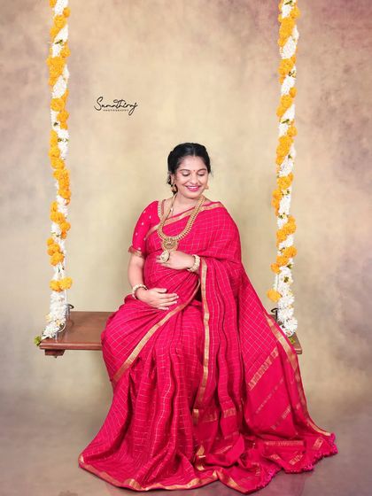 A joyful moment on a swing during a traditional saree shoot. The mother-to-be's happy expression and the festive floral decorations create a vibrant and heartwarming image.