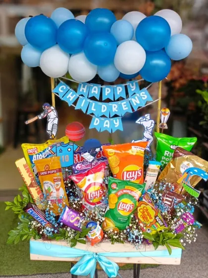 This large Children's Day hamper is packed with fun and flavor. It features a variety of chips, chocolates, and snacks, all topped with a festive balloon arrangement and cricket-themed cutouts, making it a perfect surprise for the little ones.