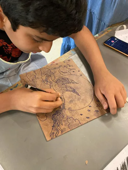 A student carves intricate details into his block for a woodcut print, showing great focus and skill.
