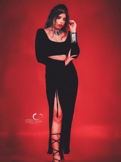 A confident and alluring pose in a black dress against a red background. The styling is simple yet powerful, focusing on her expression.