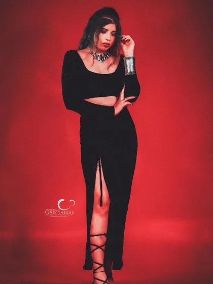 A confident and alluring pose in a black dress against a red background. The styling is simple yet powerful, focusing on her expression.