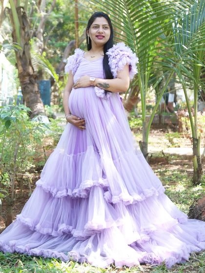The lavender ball gown stands out beautifully against the tropical foliage in this outdoor shot. The ruffled sleeves and tiered skirt create a stunning silhouette.