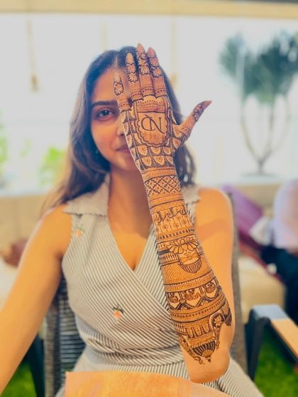 A client playfully showing off her full-arm mehandi, which features the initials "ND" on the palm.