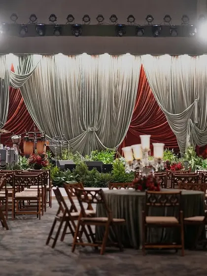 A wide shot of the sangeet stage and seating, capturing the grandeur and drama of the event. The velvet drapes and warm lighting create a truly theatrical experience.