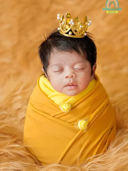 A close-up portrait of a sleeping newborn prince wearing a golden crown, wrapped in a warm yellow swaddle.