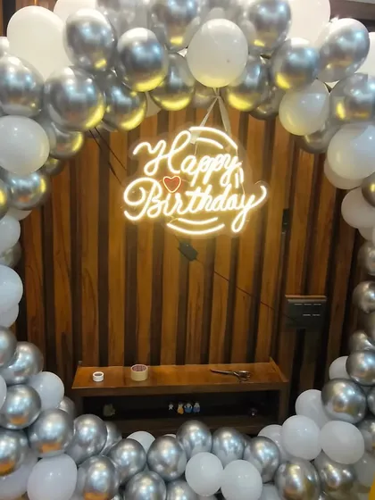 A simple and elegant silver and white balloon ring. The "Happy Birthday" neon sign with a small heart adds a lovely touch to this classic setup.