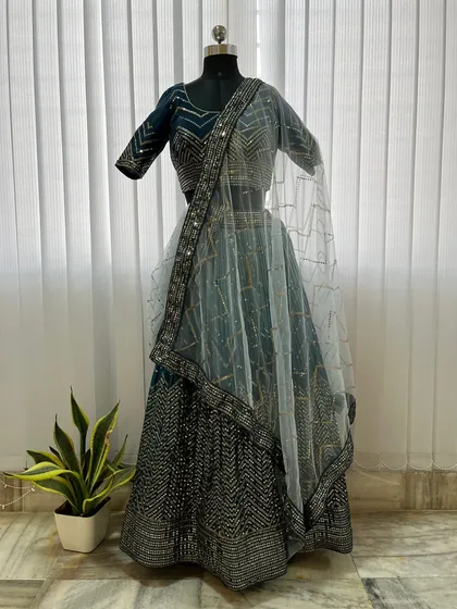 This teal blue lehenga is covered in geometric sequin work, offering a dazzling effect. Paired with a sheer dupatta, it's a modern and eye-catching rental choice for any evening celebration.