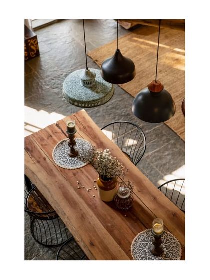 The raw wood of the dining table and the varied textures of the lights and placemats create a rich, tactile dining experience.