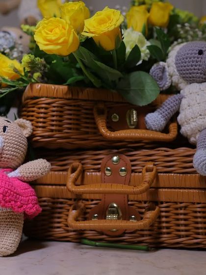 A close-up of the adorable handmade crochet teddy bear and sheep, placed on vintage-style wicker suitcases. These thoughtful details also serve as wonderful keepsakes for the parents-to-be.