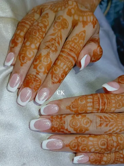 A classic French manicure with a touch of sparkle is a timeless choice for brides. The clean white tips and shimmering nude base look elegant against the henna.