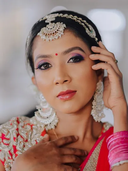 A close-up portrait of a model in a red lehenga, highlighting her makeup and jewelry. The direct gaze and pose create a confident and striking image.