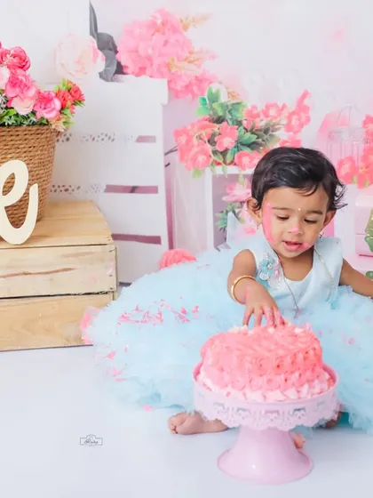 A moment of discovery during a first birthday cake smash. This little girl in a blue tutu curiously touches her pink cake, a sweet and candid shot from her special day.