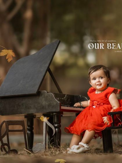 Our beautiful baby. A happy girl in a red dress plays the piano as autumn leaves fall around her.
