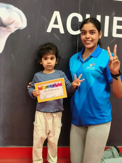 A very young student and her coach celebrate a new certificate with peace signs.