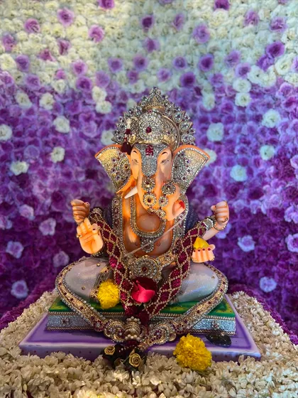 A close up of Bappa set against the purple and white ombré floral backdrop. The intricate details of the idol and the rich texture of the flowers come together to create a truly divine look.