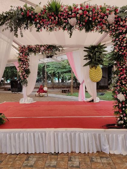 A beautiful floral mandap designed for an outdoor wedding, featuring a mix of pink and white flowers with unique pineapple-shaped floral arrangements for a tropical touch.