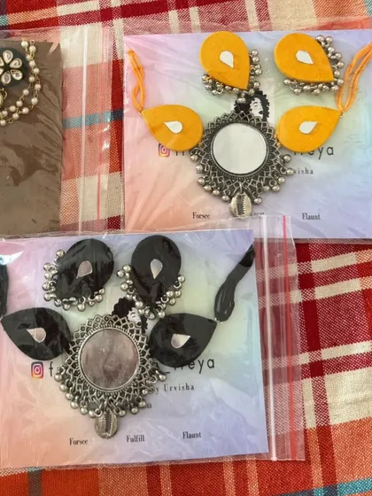 My classic mirror necklace sets are available in a range of colors like red, yellow, and black. They feature a large central mirror pendant with fabric accents and matching earrings.