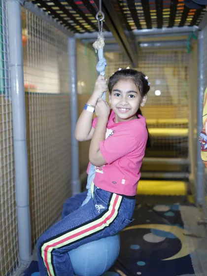 A smiling girl enjoys the ride on our ball swing, a fun feature within our multi-level play structure.