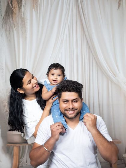 A classic family pose with the baby girl sitting on her father's shoulders, all sharing a happy moment.