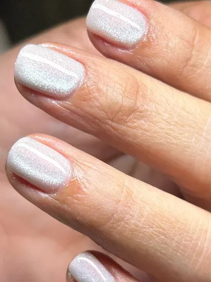 A pearly, iridescent white polish on short, natural nails. The subtle shimmer gives a 'glazed' effect that is modern and chic.