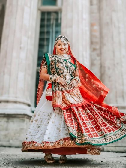 A stunning portrait of a bride in her traditional Gujarati panetar, a white and red saree. The twirling motion showcases the beauty and intricacy of her wedding lehenga.