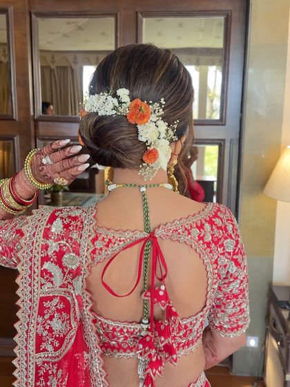 A timeless bridal bun for a wedding in Udaipur, featuring a mix of orange and white fresh flowers for a classic look.
