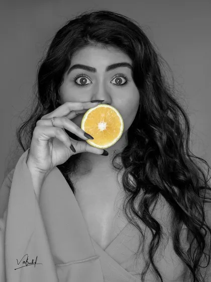 Playing with selective color in a fun, creative portrait. The bright yellow of the orange slice pops against the black and white image, drawing attention to the model's expressive eyes.