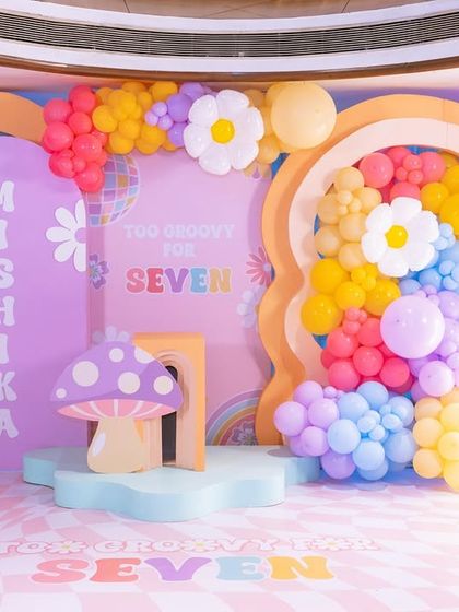 The full, vibrant backdrop for the groovy 7th birthday party, featuring a mix of pastel and bright balloons, daisies, a disco ball, and a whimsical mushroom prop.