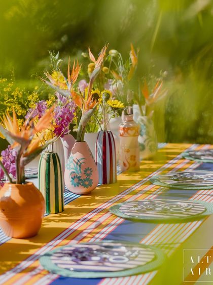 A vibrant tablescape from 'The Roots' Mehendi, featuring striped linens, hand-painted vases, and exotic flowers. The design was a striking play of tone-on-tone and print-on-print.