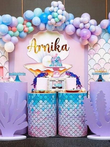 An elegant mermaid-themed setup with a pastel color palette. The decor features a seashell backdrop, scale-patterned plinths, and coral cutouts, creating a beautiful underwater scene.