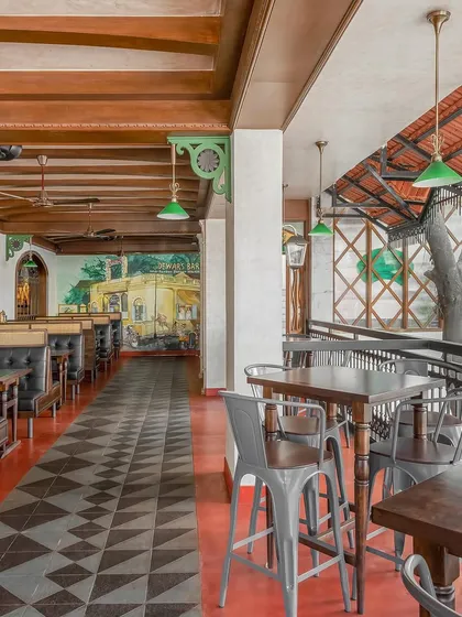The open-air seating at a restaurant, featuring a mix of industrial and traditional furniture. The design uses a red and black patterned floor and a wooden-beamed ceiling to create a rustic, charming feel.