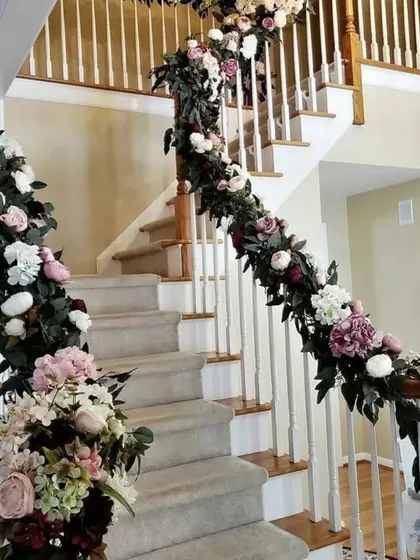 Decorating a staircase can completely transform the inside of a home for an event. Here, I wrapped the entire railing with a thick, lush garland of pink, white, and burgundy flowers, creating a stunning visual from the ground floor up.