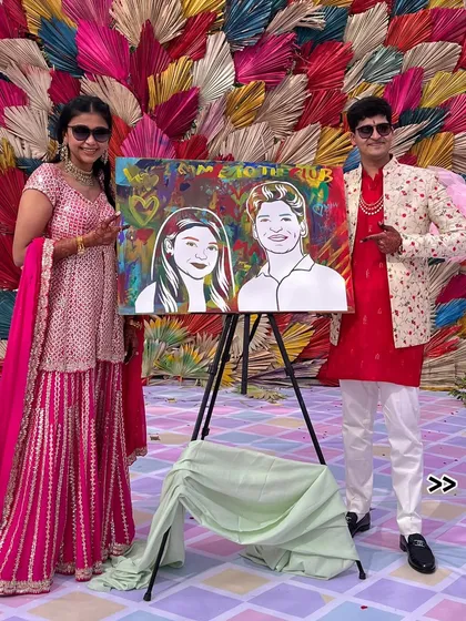 The couple posing with their portrait against a colorful backdrop. The art becomes a part of their wedding decor.