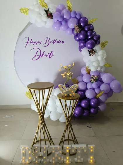 A beautiful and soft-colored theme for Dhriti's birthday. The purple and white balloon arch is accented with golden leaves and a butterfly, with the name spelled out in marquee letters at the base.