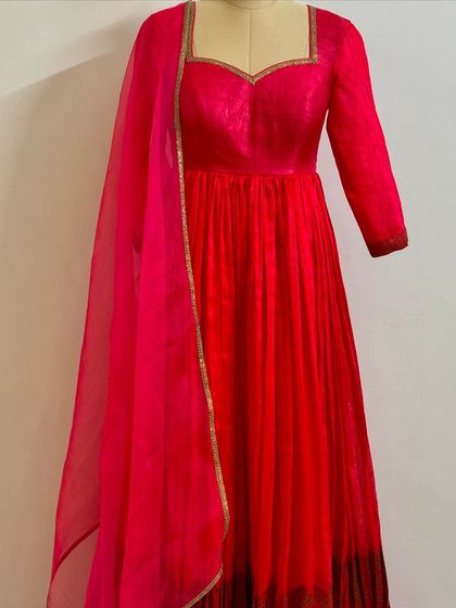 A vibrant red and pink ombre anarkali gown on a mannequin. This piece features a sweetheart neckline and a flowing pleated skirt.