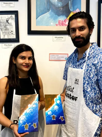 A couple with their finished canvas paintings of sea turtles. This is a great project for couples or friends to work on together.