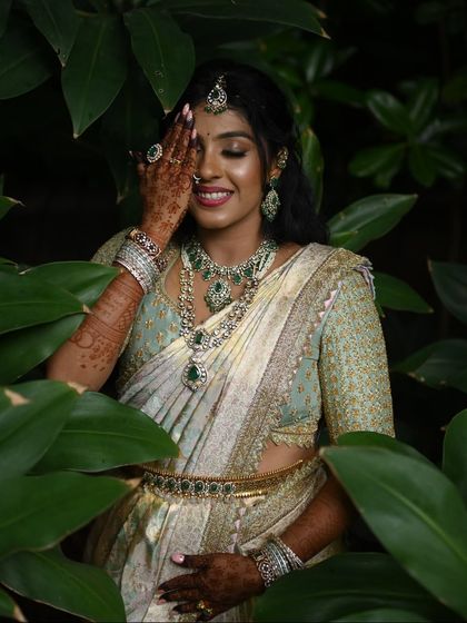 A candid moment with a happy bride. She is wearing a pastel green blouse with all-over embroidery, perfectly complementing her off-white and gold Kanchivaram saree and emerald jewelry.