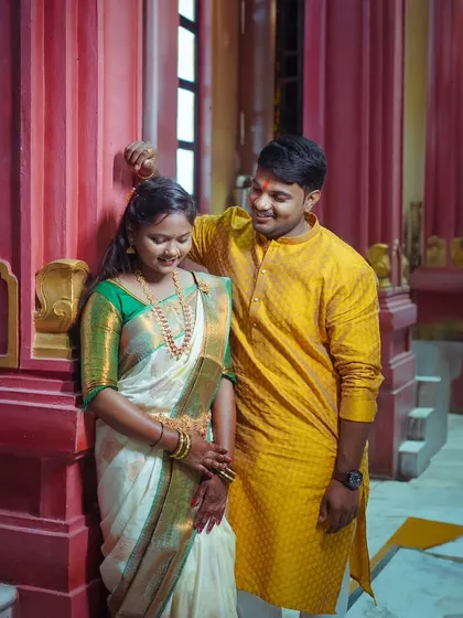A sweet, candid moment between a South Indian couple at a temple. The groom's gentle gesture and their shared smiles create a natural and heartwarming portrait.