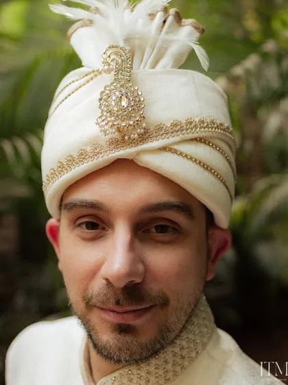 A close-up portrait of the groom, focusing on the intricate details of his wedding turban (safa). His calm expression reflects the significance of the day.