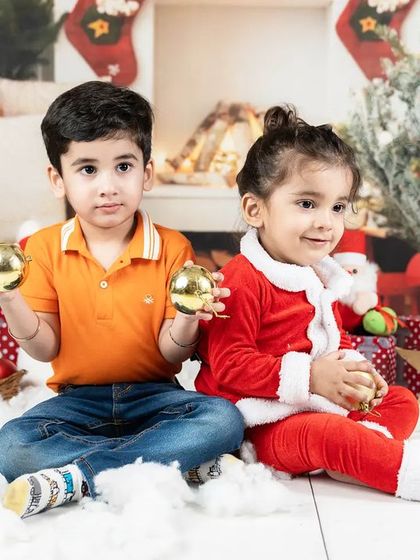 A brother and sister enjoying a Christmas-themed photoshoot, holding golden ornaments. A perfect memory for a family holiday card.