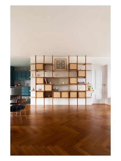 The modular birch and teak shelving unit stands as a sculptural divider, separating the living area from the kitchen while providing a dynamic display space.