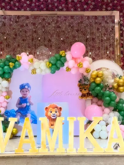 The complete stage setup for Vamika's party, with marquee letters, balloon columns topped with lioness cutouts, and a personalized backdrop.