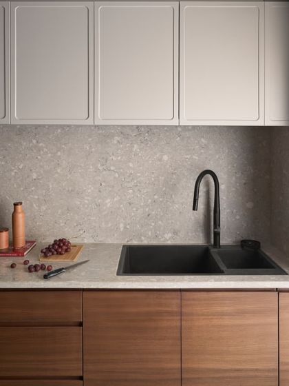 The kitchen features handleless lower cabinets in a teak finish and upper cabinets in a light grey duco finish. This two-tone approach adds visual interest while keeping the space feeling bright.