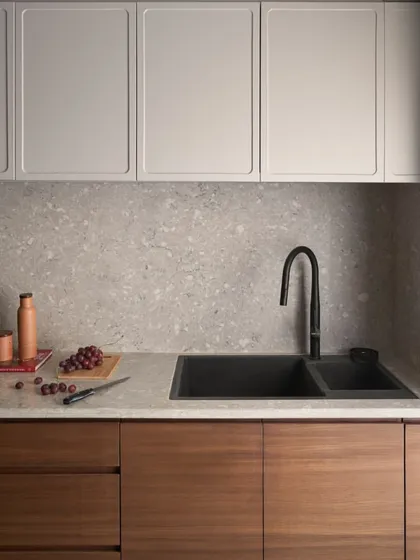 The kitchen features handleless lower cabinets in a teak finish and upper cabinets in a light grey duco finish. This two-tone approach adds visual interest while keeping the space feeling bright.