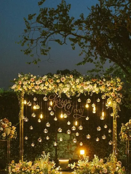 A beautiful photo backdrop for a night function, featuring a floral arch with hanging light bulbs and crystals.